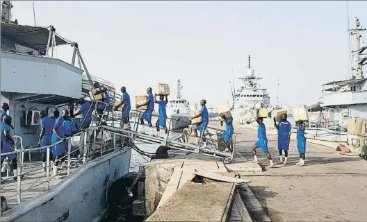  ?? LA VANGUARDIA ?? Porteadore­s. Miembros de la Marina senegalesa llevan hasta su buque ‘Goree’ lacarga del Infanta Elena, situado al fondo a la derecha