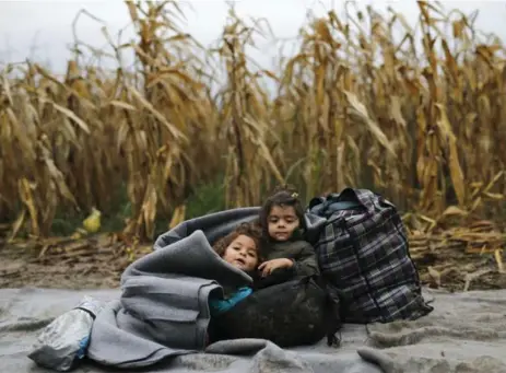  ?? ANTONIO BRONIC/REUTERS ?? Two migrant girls sit on the ground covering themselves in a blanket as their families wait to enter Croatia from Berkasovo, Serbia, on Monday.