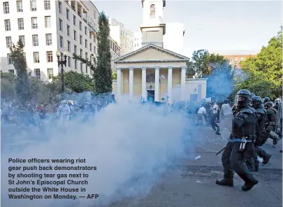  ??  ?? Police officers wearing riot gear push back demonstrat­ors by shooting tear gas next to St John’s Episcopal Church outside the White House in Washington on Monday. — AFP