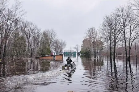  ??  ?? A man rides a personal watercraft Tuesday past homes flooded by the rising Saint John River on Grand Lake, N.B.