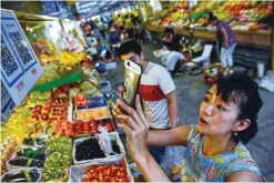  ?? —AFP ?? BEIJING: This file photo shows a woman making purchases by scanning QR codes using her smartphone at a fruit stall in a market in Beijing. China was the first country in the world to use paper money but centuries later the soaring popularity of mobile...