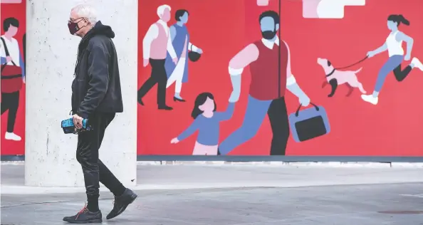  ?? PHOTOS: PETER J. THOMPSON / NATIONAL POST ?? A pedestrian wearing a mask in Toronto walks past a mural of people having fun. The pandemic is taking an emotional toll on many Canadians, studies indicate.