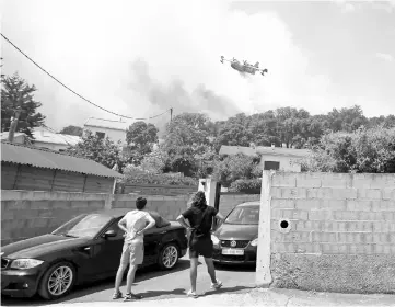  ?? — AFP photo ?? People look at a Canadair aircraft dropping water over a fire in Ortale di Biguglia, near Biguglia, on the French Mediterran­ean island of Corsica.