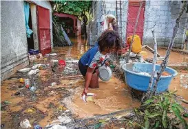  ??  ?? Yoleine Toussaint, 22, removes mud from plates in front of her flooded house Monday after Tropical Storm Laura slammed Port-au-Prince, Haiti.