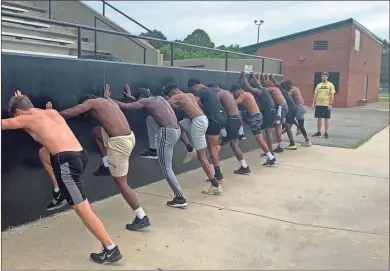  ?? Contribute­d ?? A group of Rockmart High School football players stretch against the wall of the home stands of the football stadium during conditioni­ng workouts in early June. Head coach Biff Parson said they are seeing good progress though they’ve had to adapt their summer workouts.