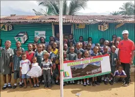  ??  ?? Co-founder of Library for Africa, Darius Ricks, stands with students from Ardju Preparator­y and Daycare Center holding a banner for the future Library of Liberia.
