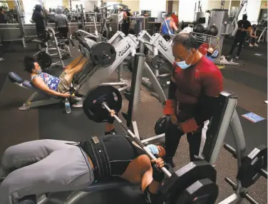  ?? Photos by Lea Suzuki / The Chronicle ?? Dillon Alvarado lifts weights as Daniel Castillo spots him, above, at 24 Hour Fitness in Redwood City on Friday. Gyms and nail salons, below, in the city will close if San Mateo County joins the state’s watch list.