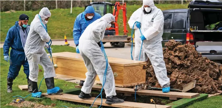  ??  ?? Safety measures: Ismail Mohamed Abdulwahab’s coffin is lowered into the ground by mourners in protective suits and face masks at his funeral in south London yesterday