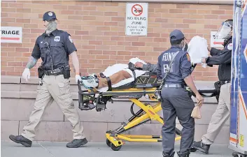  ?? — AFP photo ?? Medical workers take in patients outside a special coronaviru­s area at Maimonides Medical Center as the US surpasses 100,000 fatalities from Covid-19 in New York City.