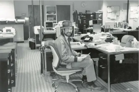  ?? STAFF FILE ?? Columnist Pat Lackey at his desk, wearing a Virginian-Pilot/Ledger-Star hat. The computer monitors are “dumb” video display terminals, connected to a mainframe computer, and the internet didn’t exist.