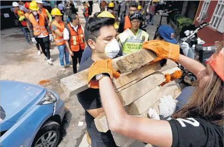  ?? Photograph­s by Gary Coronado Los Angeles Times ?? VOLUNTEERS transport wood to help shore up Enrique Rebsamen school in Mexico City amid search efforts at the collapsed building.