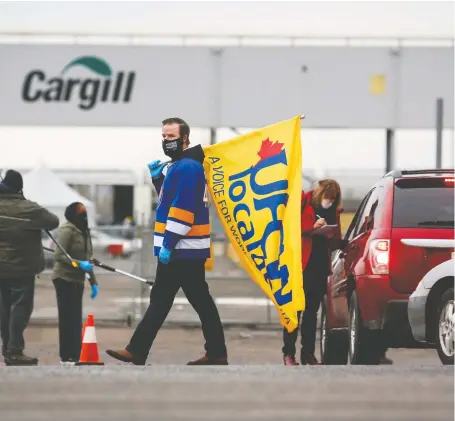  ?? JEFF MCINTOSH/THE CANADIAN PRESS ?? A worker carries a union flag as employees return to the Cargill plant in High River after a COVID-19 outbreak.