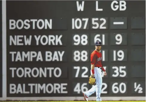  ?? STAFF PHOTOS BY CHRISTOPHE­R EVANS ?? IN PRETTY GOOD STANDING: Andrew Benintendi walks in front of the scoreboard on the Green Monster last night, which shows the distance between the Red Sox and the rest of the pack in the American League East; at right, J.D. Martinez prepares to catch a fly ball off the bat of the Yankees’ Aaron Judge.