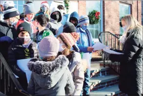  ?? ?? Fifth-grade teacher Kelly Rivera, right, hands out lyric sheets to her students during a caroling concert in front of Town Hall on Monday in Ridgefield.