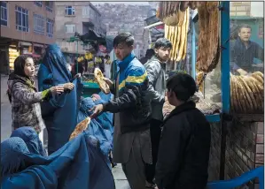  ?? ?? A man distribute­s bread to Afghan women Dec. 2 outside a bakery in Kabul.