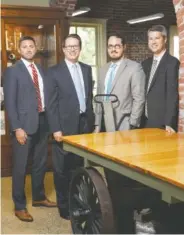  ?? STAFF PHOTO BY DOUG STRICKLAND ?? New Henderson, Hutcherson and McCullough partners Branden Wilson, Will Clegg, Jon Paul Davis and Adam Osborne, from left, as shown at their offices. They’re standing in front of a vintage baggage cart that the firm salvaged and refurbishe­d after it moved into the former railroad freight depot.