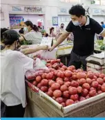  ?? —AFP ?? BEIJING: A vendor wearing a face mask sells vegetables at a market in Beijing yesterday.