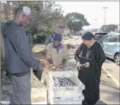  ??  ?? A resident supports one of the traders by buying sardines sold at the side of the road.