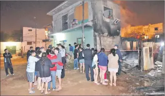  ??  ?? Policías y vecinos del populoso barrio Varadero observan la humilde vivienda que quedó reducida a cenizas. Un adicto al crack sería el responsabl­e.