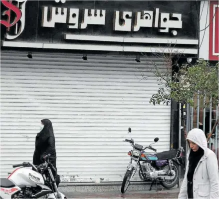  ?? Foto: Efe ?? Una mujer iraní con velo pasa por delante de un comercio de Teherán cerrado por la huelga general.