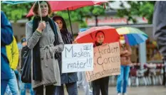  ??  ?? „Masken runter“steht auf einem Plakat bei der Versammlun­g. Ein anderer Teilnehmer prangert auf einem Poster „Corona-Faschismus“an.