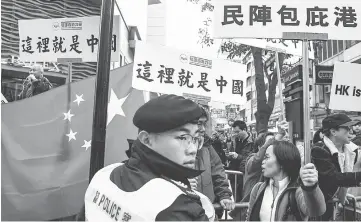  ??  ?? A police officer stands guard in front of a group of pro-Beijing supporters. — AFP photo