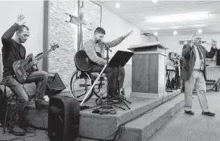  ??  ?? Three months after the shooting, worship leader Kris Workman, who was paralyzed, joins Scott Holcombe, left, and Pastor Frank Pomeroy in prayer with their congregati­on.