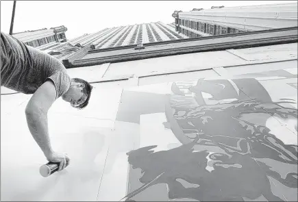  ?? PHOTOS BY MIKE BROWN/THE COMMERCIAL APPEAL ?? Artist Kyle Taylor works on a mural at the base of the Sterick Building, a long-vacant 29-story tower located Downtown. Images include corporate logos of big companies that had offices there and constructi­on of the Hernando DeSoto Bridge, which Sterick...