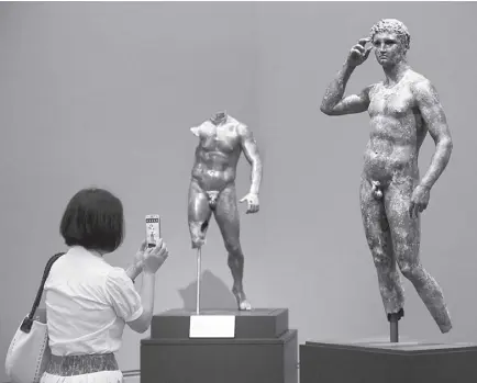  ?? AP ?? REPORTER Sookee Chung takes a photo of a sculpture titled Statue of a Victorious Youth, 300-100 B.C. at the J. Paul Getty Museum in Los Angeles, on July 27, 2015. A European court upheld Italy’s right to seize a prized Greek statue from the J. Paul Getty Museum in California.