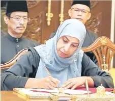  ?? — Bernama photo ?? Latheefa signs the documents to mark her official appointmen­t as the new MACC chief commission­er.
