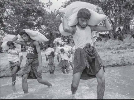  ?? AP PHOTO ?? Rohingya Muslims, who recently crossed over from Myanmar, carry food items across from Bangladesh’s border toward no man’s land where they have set up refugee camps in Tombru, Bangladesh.