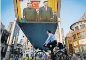  ?? [AP PHOTO] ?? People bicycle past a giant TV screen broadcasti­ng the meeting of North Korean leader Kim Jong Un and Chinese President Xi Jinping on Tuesday during a welcome ceremony at the Great Hall of the People in Beijing.