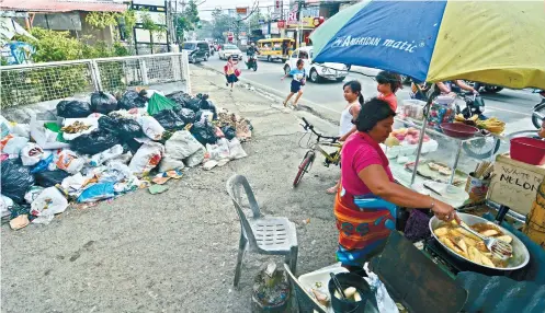  ??  ?? A banana cue vendor goes about her chores, not minding the heap of garbage behind her in Barangay Guadalupe, Cebu City.