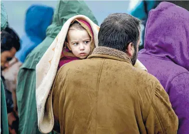  ??  ?? A man holds a child covered in a blanket while waiting in line Wednesday for food during rainfall at the northern Greek border station of Idomeni.