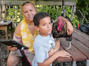  ?? MELANIE STENGEL/C-HIT ?? Susana Encarnacio­n of New London holds an iPad that the city school system supplied for her son, Jeremiah, a 9-year-old who is going into fourth grade this fall, to do his online lessons. Next to her, Jeremiah is holding the family’s rooster, “Old Man.”