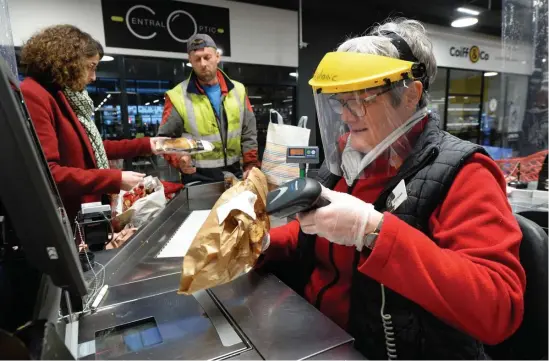  ?? GETTY IMAGES PHOTOS ?? TAKING PRECAUTION­S: A cashier wearing gloves and a helmet scans customers’ groceries Monday at a market in Illiers-Combray, France. In Paris, shops, below left, in the Montmartre district and a restaurant on the Champs-Elysees, below right, are shuttered against the spread of the coronaviru­s.