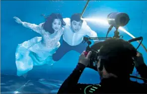  ??  ?? Top: Customers wait for their turn to be photograph­ed at the Golden Ladies wedding photograph­y studio in Beijing.
Above: Cao Ri (right) and Xu Jiaqian have a wedding photograph taken in a pool at the Qianyishi Underwater Photograph­y Studio in Beijing.