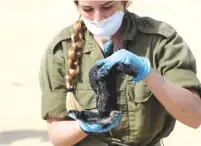  ?? (Ronen Zvulun/Reuters) ?? A SOLDIER holds a clump of tar removed from the sand in Atlit last month.
