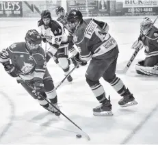  ??  ?? Elmira’s Zach Cameron, backed up by Damian Figueira, looks to clear the puck away from the danger zone during game action in Stratford.