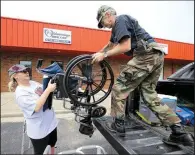  ?? Arkansas Democrat-Gazette/STEPHEN B. THORNTON ?? Jennifer Crismon hands a wheelchair to Ravenden Springs Mayor John Cochran outside her homecare store Wednesday in Pocahontas. Crismon was delivering items to elderly people riding out the flood at a shelter. At right, a basketball goal barely sticks...