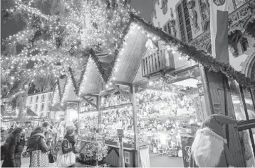  ?? THOMAS LOHNES/GETTY-AFP ?? People stroll the Christmas market Tuesday in Frankfurt, Germany. Despite the pandemic inconvenie­nces, stall owners selling ornaments, roasted chestnuts and other items in European cities are relieved to be open at all.