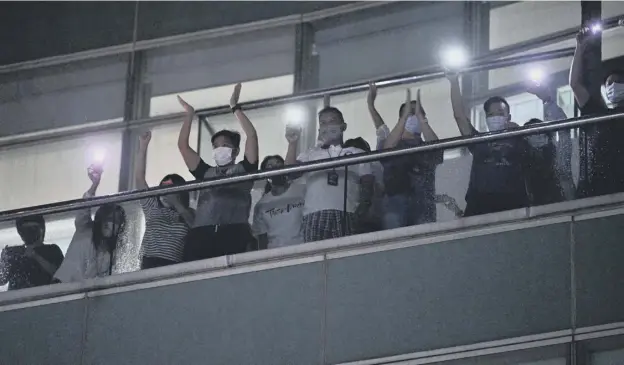  ??  ?? Employees of the Apple Daily newspaper shine phone torches and applaud from an office balcony while shouting thanks to supporters down on the street below