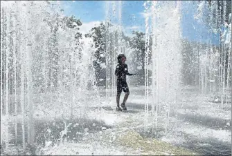  ??  ?? Un enfant se rafraîchit dans des jets d’eau lors d’un épisode de canicule.