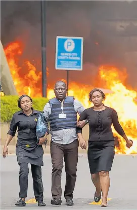  ?? Photos / AP ?? A member of the security forces helps civilians flee as cars burn behind at a hotel complex in Nairobi, Kenya.