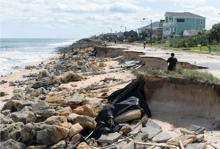  ??  ?? ONLOOKERS VIEW a washed-out portion of State Highway A1A in the aftermath of Hurricane Matthew in Flagler Beach, Florida, last week.