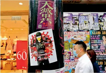  ?? — AP ?? A man walks past the stickers with messages about an anti-Beijing government that were left by protesters on a street in Hong Kong, on Thursday. Police have made the first arrests under a new national security law imposed by mainland China, as thousands of people defied tear gas and pepper pellets to protest against it. Police say they arrested 10 people under the law, including at least one who was carrying a Hong Kong independen­ce flag.