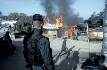  ?? THIBAULT CAMUS/ASSOCIATED PRESS ?? A man walks past a burning house in the makeshift migrant camp known as “the jungle” near Calais, France, on Tuesday. Crews have started dismantlin­g the migrant camp after the process to clear migrants began Monday.