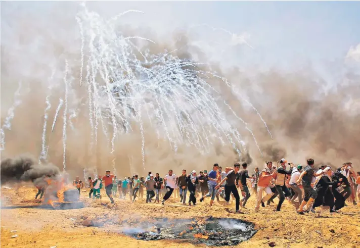  ??  ?? ► Palestinos huyen de las bombas de gas lacrimógen­o durante los enfrentami­entos con las fuerzas de seguridad israelíes cerca de la frontera, al este de Jabalia.