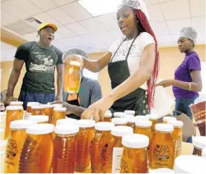  ?? PHOTOS BY JOE BURBANK/STAFF PHOTOGRAPH­ER ?? Erika Bearden, on quality control, discovers a label problem to Daquan Evans’ surprise on production day at Black Bee Honey, based at the Callahan Neighborho­od Center in Orlando. Above, Daquan packages honey. Black Bee is a non-profit business teaching...