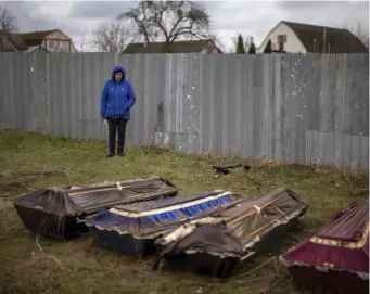  ?? Ap FILE ?? LOVED ONES: Ira Slepchenko, 54, stands next to coffins, one of them with the body of her husband Sasha Nedolezhko, 43, during an exhumation of a mass grave in Mykulychi, Ukraine on April 17. All four bodies in the village grave were killed on the same street, on the same day. Their temporary caskets were together in a grave. On Sunday, two weeks after the soldiers disappeare­d, volunteers dug them up one by one to be taken to a morgue for investigat­ion.